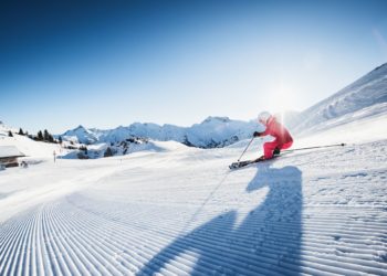 Ein Skifahrer im roten Skidress auf der Piste bei Sonnenschein, im Skigebiet Lech Zürs am Arlberg