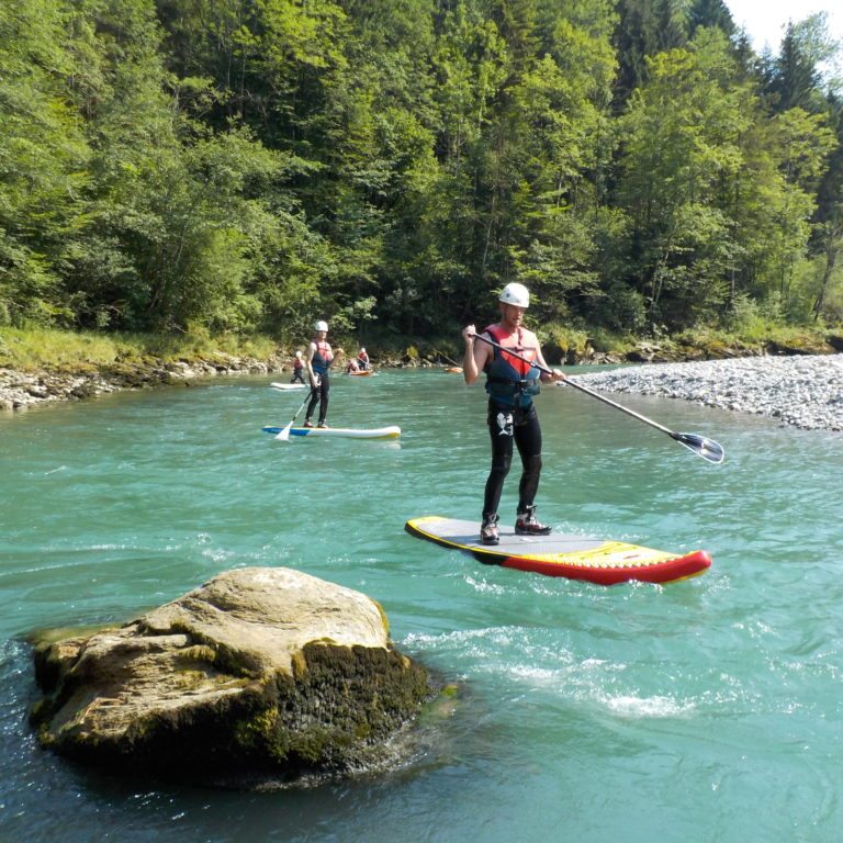 Eine Gruppe fährt Stand Up Paddle auf der Bregenzerach, ausgerüstet mit Helm und Schwimmweste, unter Anleitung von einem professionellen Guide (c) Canyoning Team Vorarlberg