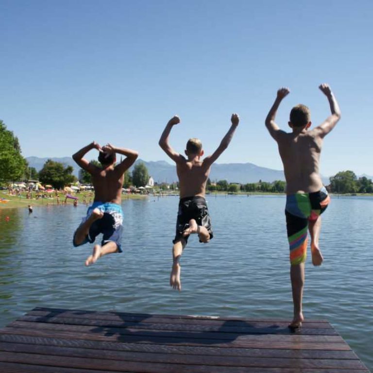 Drei Jugendliche springen von einem Holzsteg in den See im Strandbad in Hard am Bodensee
