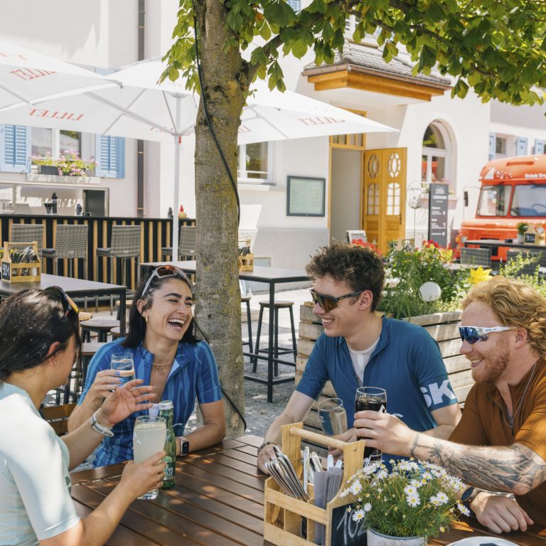 Vier Rennradfahrer:innen genießen eine Pause in einem schattigen Gastgarten im Montafon in Vorarlberg.