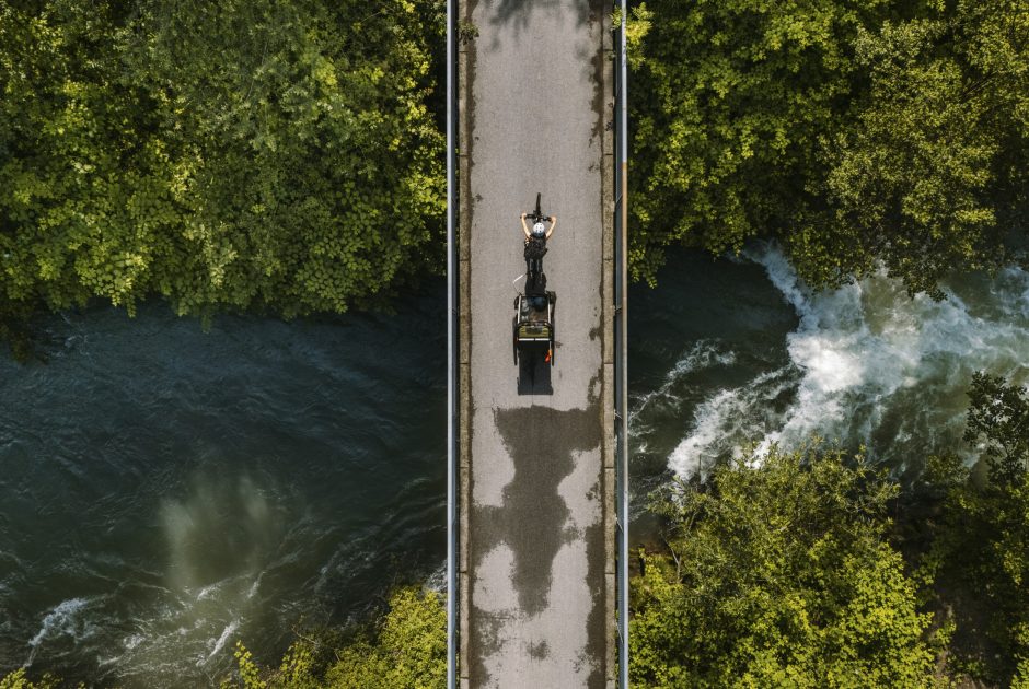 Sicht aus der Vogelperspektive: Ein Radfahrer mit Radanhänger fährt über eine Brücke, unter der ein Fluss fließt.