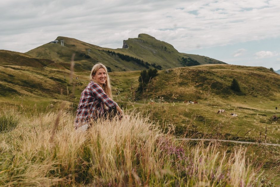 Nina Loos vom Blog Reisehappen sitzt in den Wiesen der Bregenzerwälder Berglandschaft.