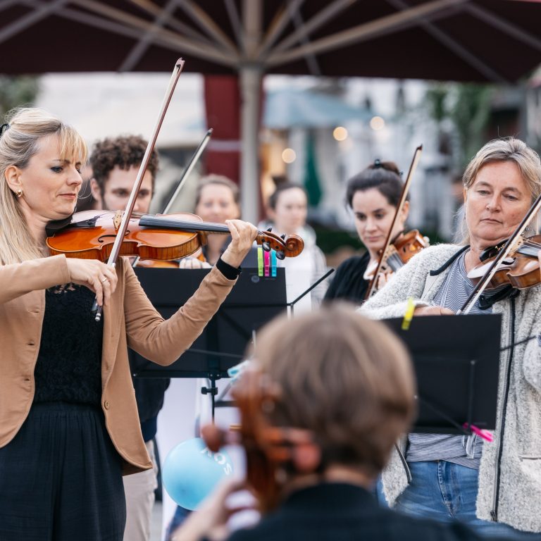 Musikerinnen mit Geigen spielen im Freien, Zuhörer:innen rundherum bei OUTREACH, einem, neuen Konzertformat des Symphonieorchester Vorarlberg