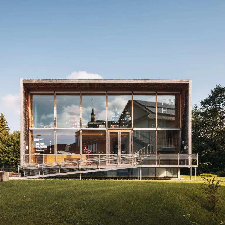 Frauenmuseum Hittisau Aussenansicht, In der Glasfassade spiegelt sich die Kirche u.a. Gebäude