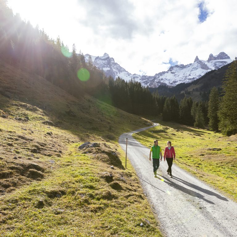 Zwei Wanderer im herbstlichen Montafon auf einem Wanderweg unterwegs, im Hintergrund verschneite Berge