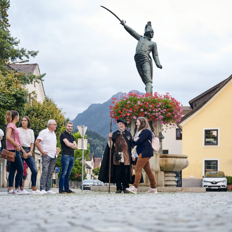 Nachtwächterführung durch Bludenz, Menschen stehen vor dem Brunnen und hören der Führung zu, Öffentliche Kulturführungen, Stadtführung in Vorarlberg