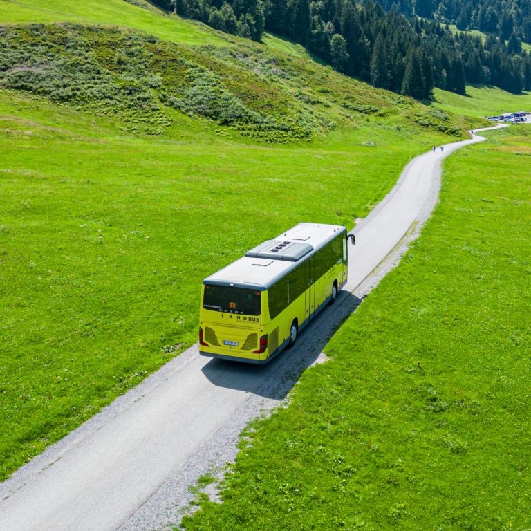 Ein Landbus auf der idyllischen Straße Richtung Schönenbach im Bregenzerwald, umgeben von grünen Feldern und bewaldeten Hügeln