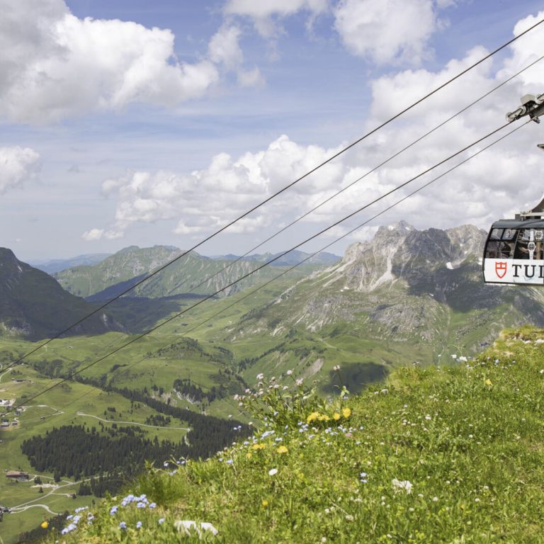 Kabine der Rüfikopfbahn 1 in Lech am Arlberg, darunter blühende Sommer-Berglandschaft