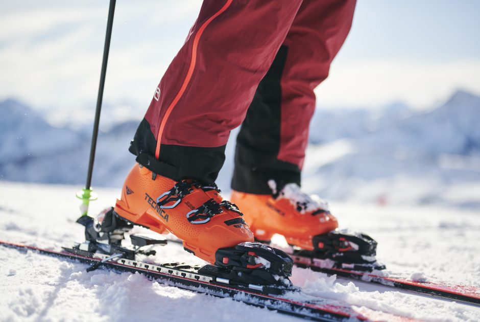 Ein Skifahrer schnallt gerade seine Ski an, er trägt orangefarbene Skischuhe.