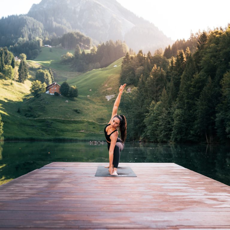 Eine Frau führt eine Yoga Übung aus, auf einem Steg beim Seewaldsee im Biosphärenpark Großes Walsertal