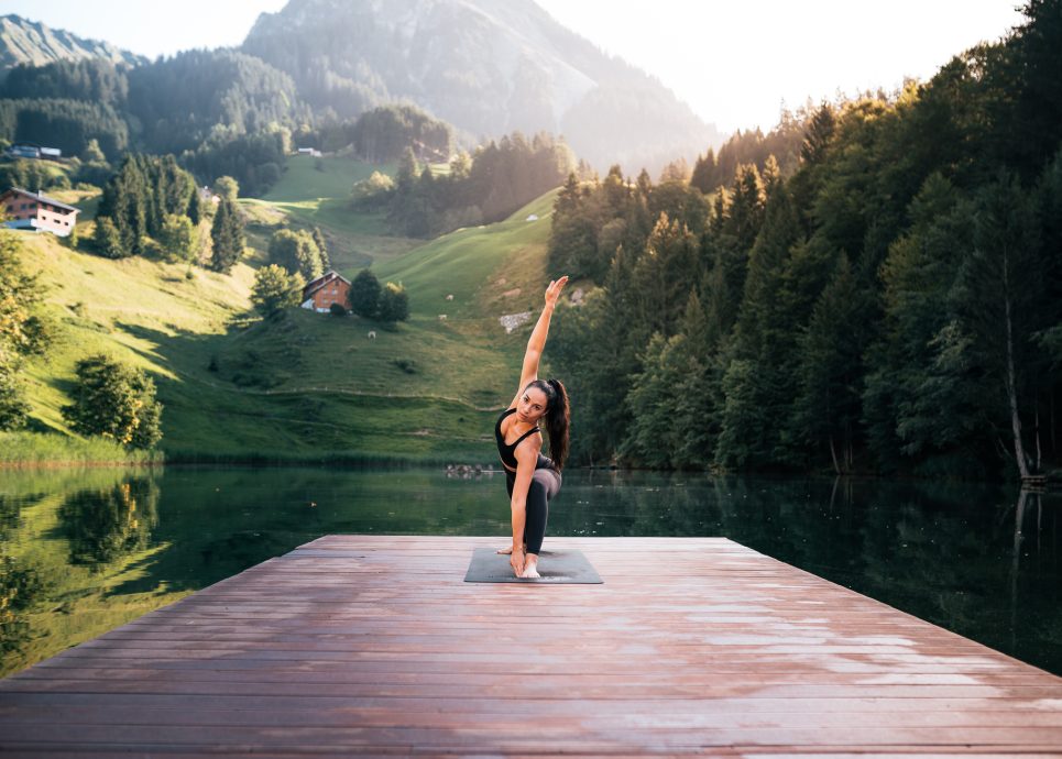 Eine Frau führt eine Yoga Übung aus, auf einem Steg beim Seewaldsee im Biosphärenpark Großes Walsertal