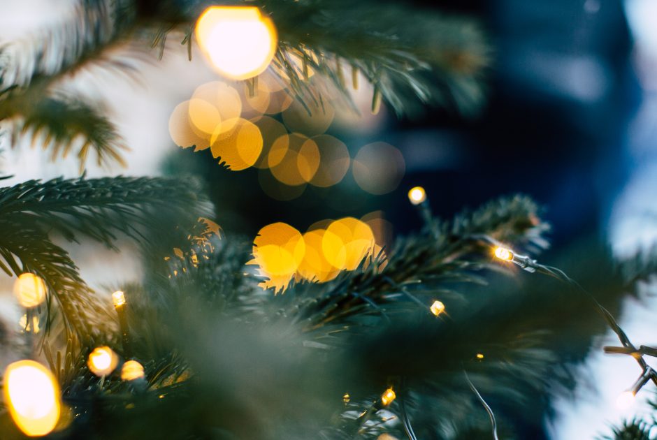 Blick durch Tannenzweige im Vordergrund auf verschwommene Christbaumkugeln und Licher am Weihnachtsbaum. Auf dem Bild steht geschrieben: Wir sagen danke