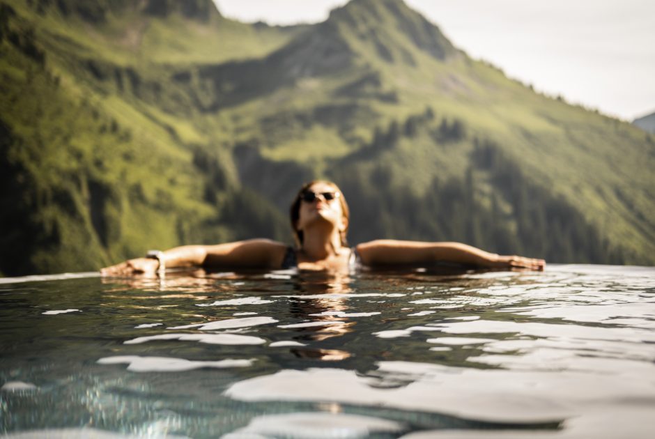 Eine Frau entspannt während ihres Wellnessurlaubs im Pool, im Hintergrund sind die Bregenzerwälder Berge zu sehen.
