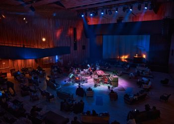 Ein Percussionist spielt inmitten von rund angeordneten Konzertbesuchern, zahlreiche Percussion Instrumente sind auf der Bühnenfläche aufgebaut