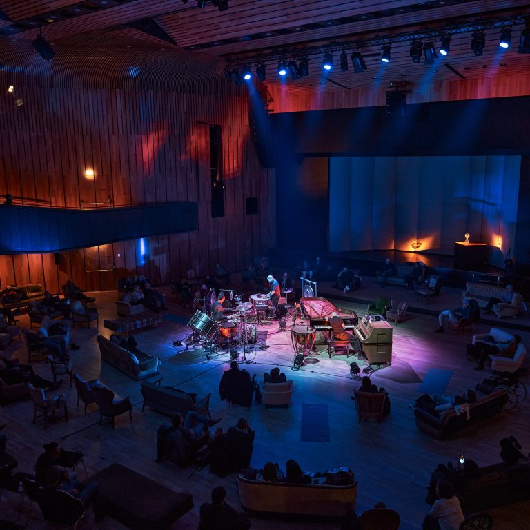 Ein Percussionist spielt inmitten von rund angeordneten Konzertbesuchern, zahlreiche Percussion Instrumente sind auf der Bühnenfläche aufgebaut, cultural events