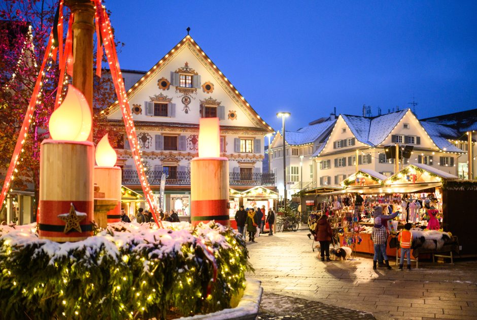 Christkindlmarkt am Marktplatz in Dornbirn, im Vordergrund ein großer Adventkrant, im Hintergrund Besucher:innen an beleuchteten Ständen