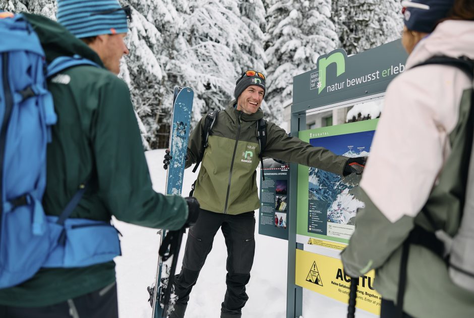 Ein Ranger mit Skiern in der Hand, erklärt anhand eines aufgestellten Schildes den Teilnehmern Wissenswertes