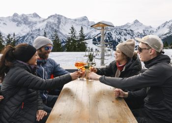 Menschen sitzen am Tisch des Restaurants Frööd, im Hintergrund schneebedeckte Berge