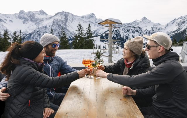 Menschen sitzen am Tisch des Restaurants Frööd, im Hintergrund schneebedeckte Berge