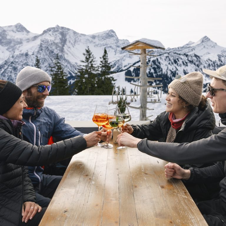 Menschen sitzen am Tisch des Restaurants Frööd, im Hintergrund schneebedeckte Berge