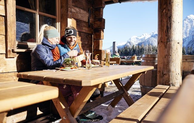 Zwei Menschen sitzen an einem Holztisch bei einer winterlichen Pause im Skigebiet Brandnertal