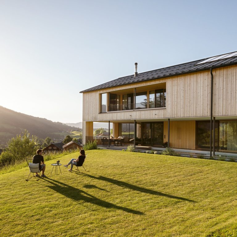Zwei Personen sitzen vor einem modernen Holzhaus im Bregenzerwald.