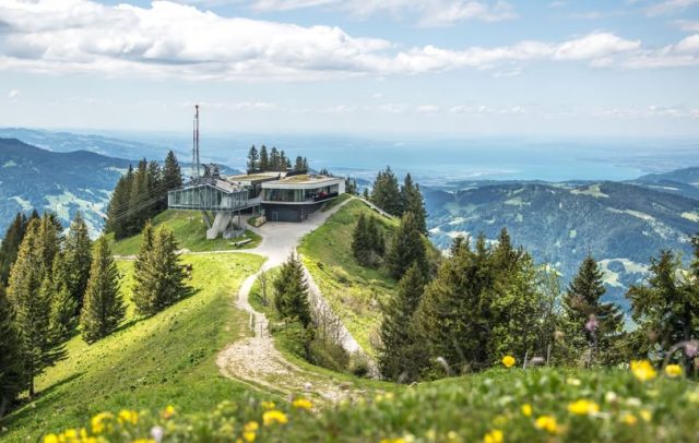 Die Bergstation Baumgarten der Seilbahnen Bezau im Frühling, im Hintergrund ist der Bodensee zu erkennen, blühende Frühlingswiesen mit Wanderwegen im Vordergrund