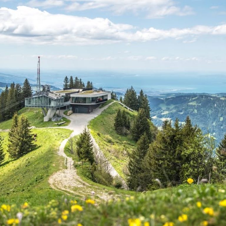 Die Bergstation Baumgarten der Seilbahnen Bezau im Frühling, im Hintergrund ist der Bodensee zu erkennen, blühende Frühlingswiesen mit Wanderwegen im Vordergrund