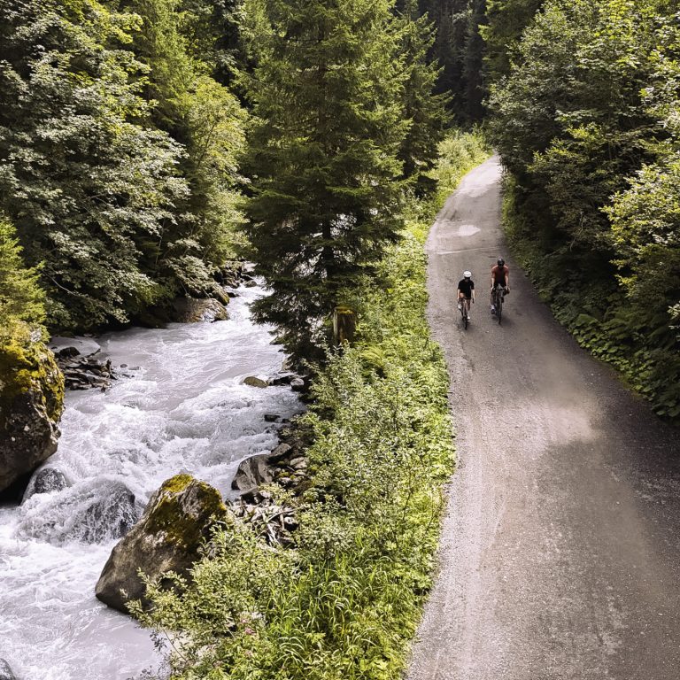 Zwei Radfahrende auf einer schattigen Straße entlang eines Gebirgsbachs in Vorarlberg